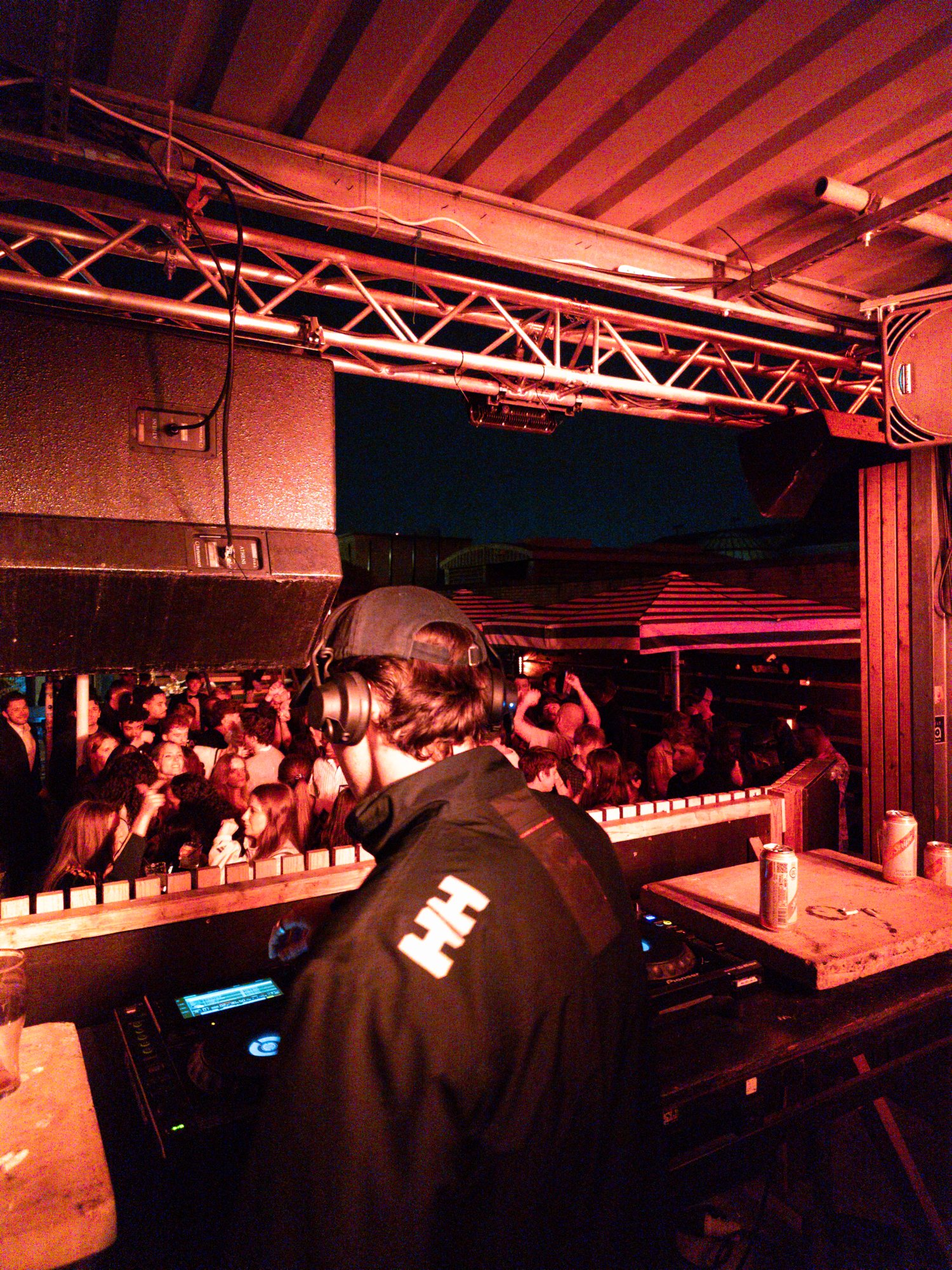 Tom (Wax Thief) on the decks, seen from behind, playing to a packed club under red light